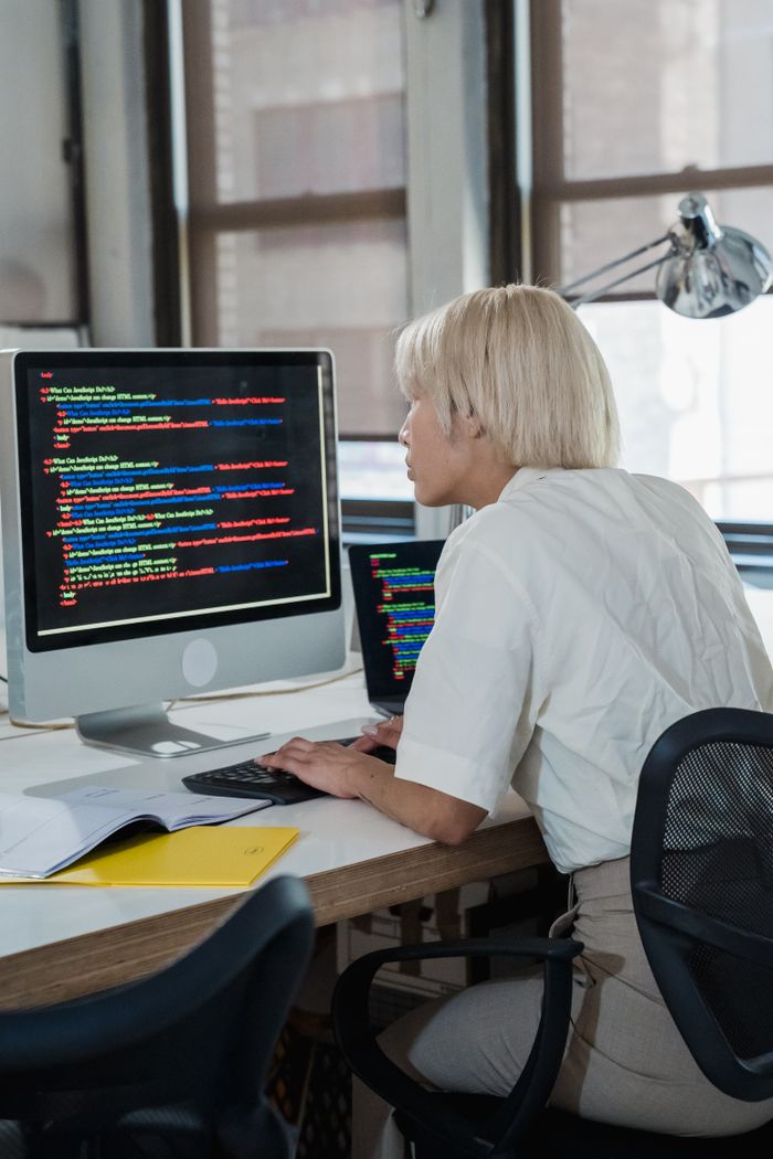 about-002 Woman engaged in software programming in a contemporary office setting with multiple screens.