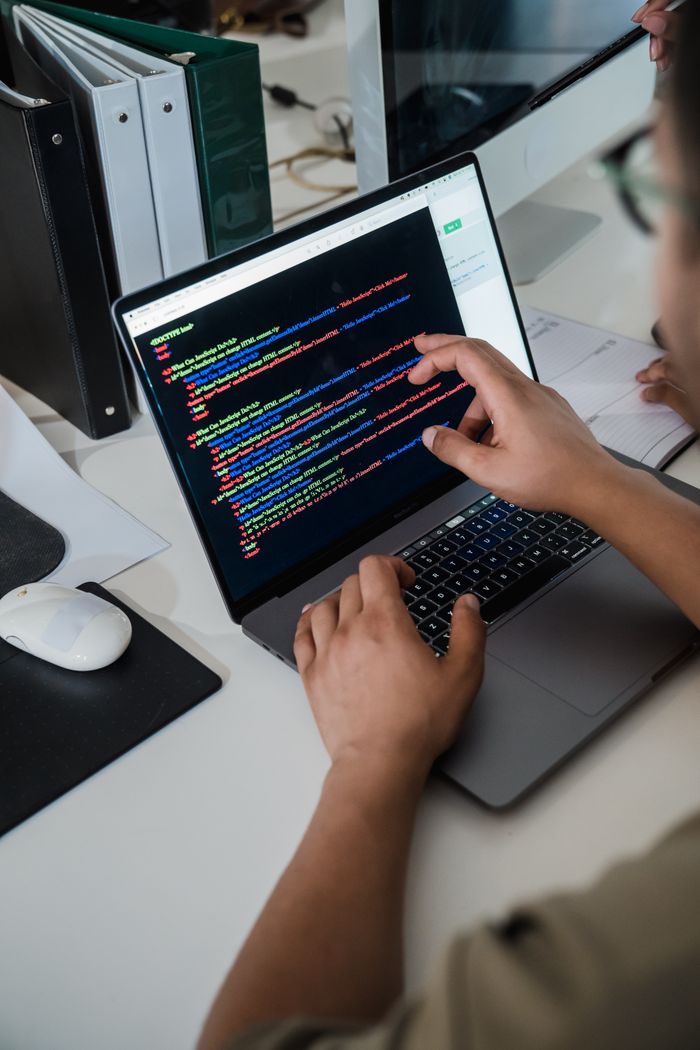 about-04 Close-up of a programmer pointing at a colorful code script on a laptop in an office setting.