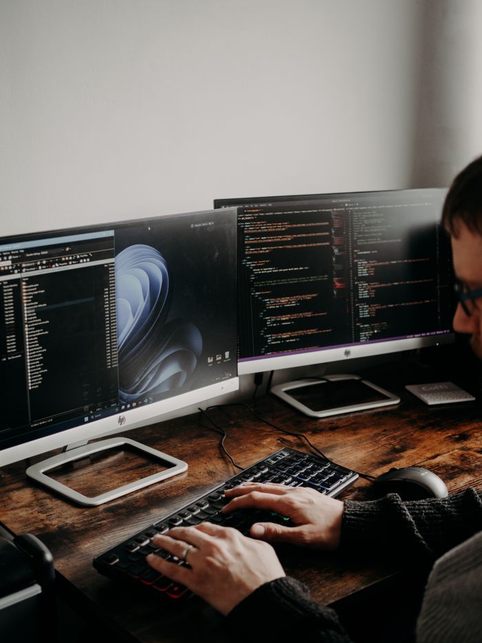 Crafting Captivating Headlines: Your awesome post title goes here A man working on website design and coding at a home office with a dual monitor setup.